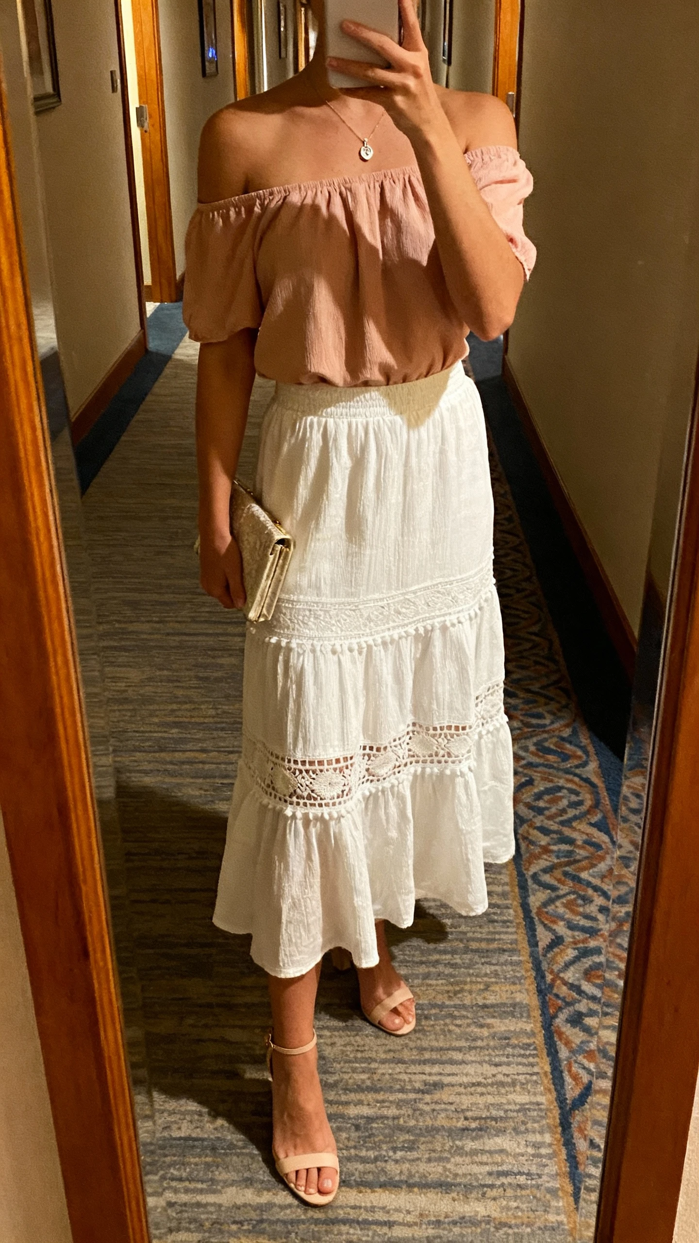 iPhone back-view selfie of a woman wearing a white boho skirt with a romantic off-shoulder blush top, delicate heels, dainty pendant necklace, small clutch, face not visible, hotel hallway mirror before an event, warm evening lighting, natural iPhone photo.