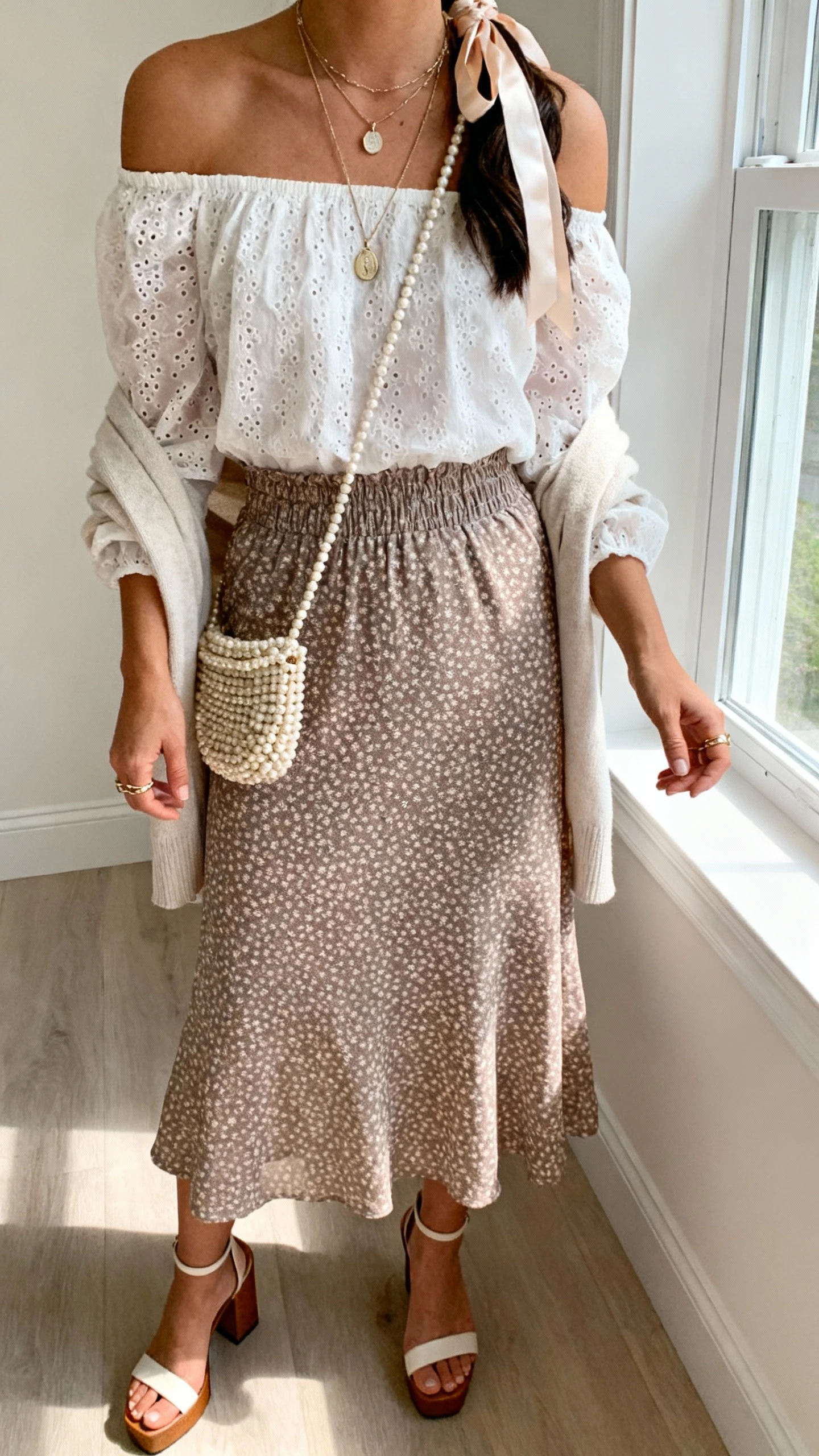 iPhone cafe table selfie cropped at shoulders of a woman in a smocked waist midi skirt (micro-floral/dotted), off-shoulder peasant blouse (eyelet/gauze), block-heel sandals, beaded crossbody bag, layered pendant necklaces and dainty rings, silk ribbon in hair with light cardigan over shoulders, face not visible, window light, casual iPhone photo.