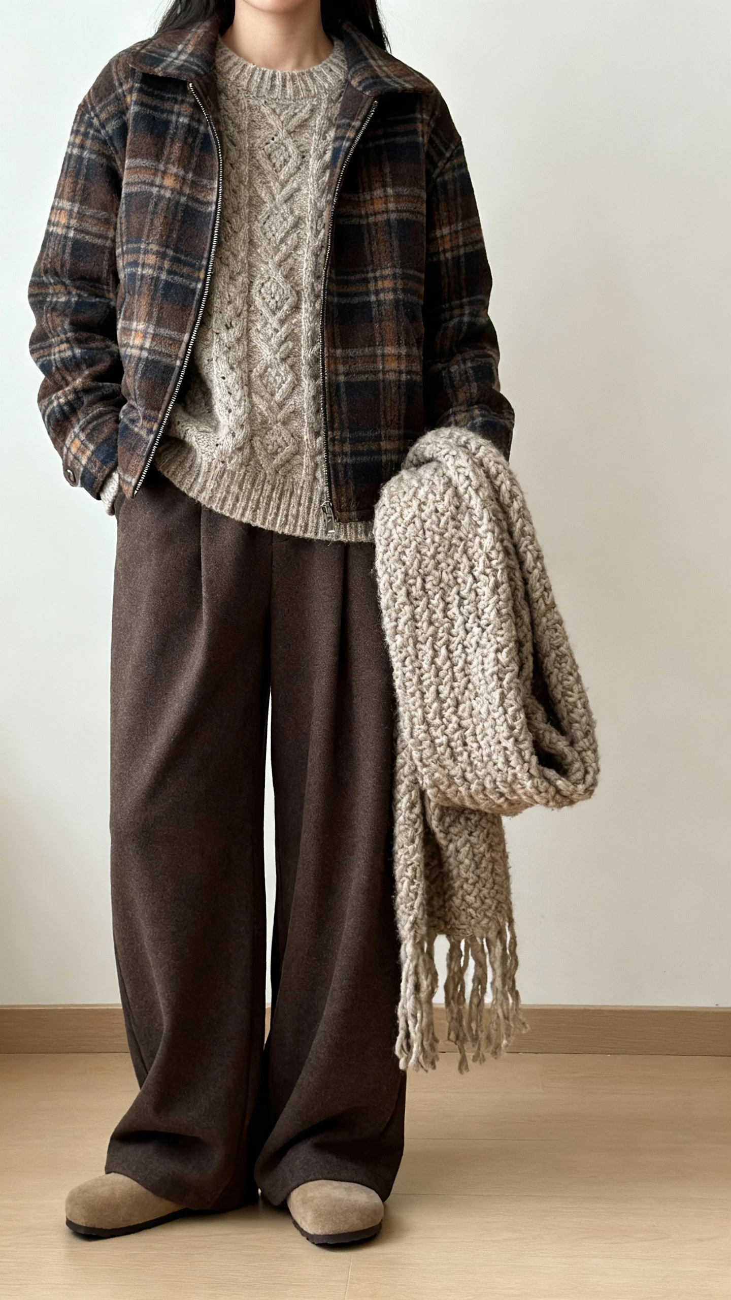 iPhone hallway mirror selfie of a woman in an artsy textured knit layered under a plaid shacket with wide-leg trousers, chunky scarf tossed over arm, clogs, face not visible, cropped at shoulders, soft indoor lighting, natural iPhone aesthetic