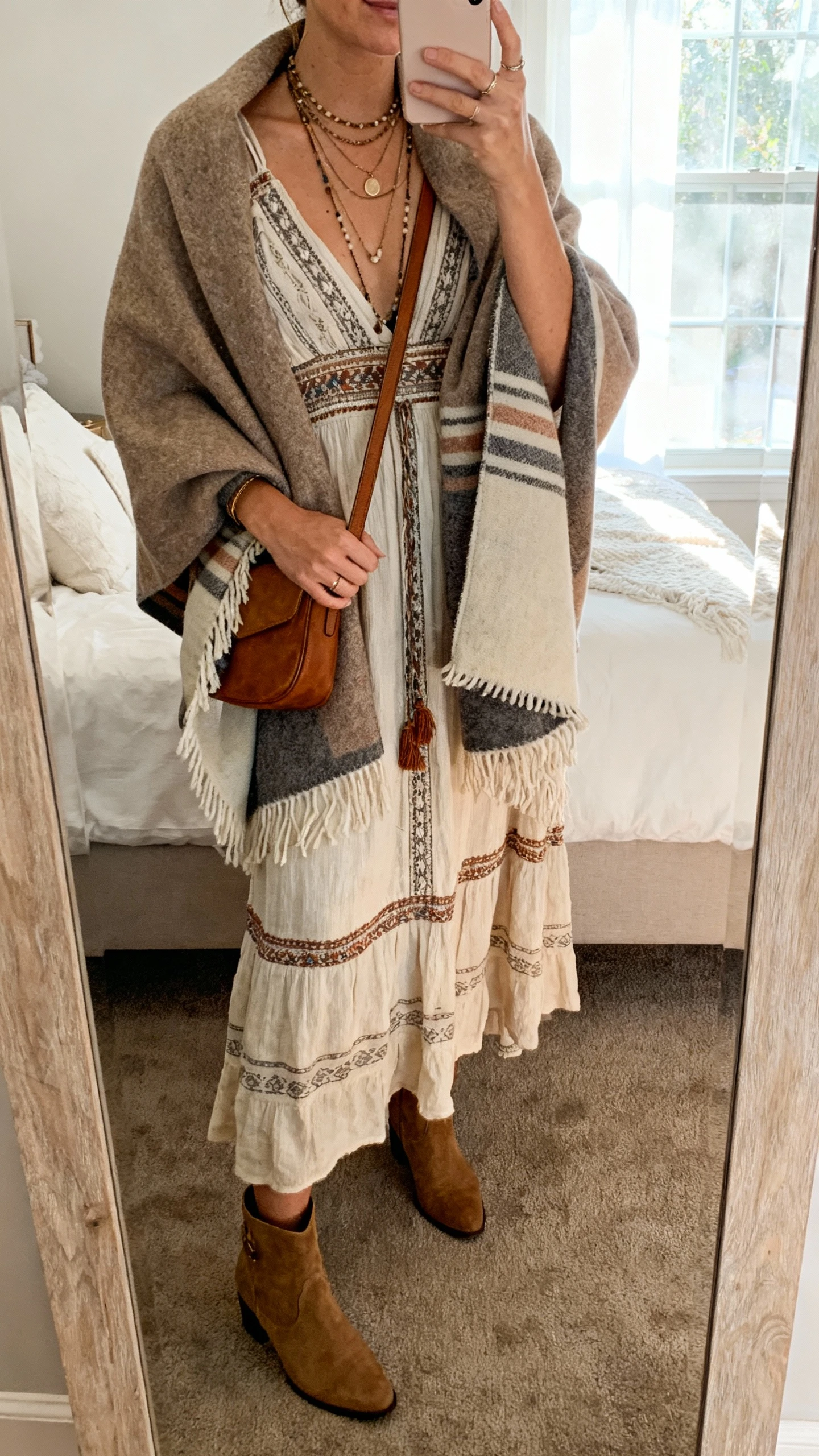 iPhone mirror selfie of a woman wearing a blanket shawl draped over a boho maxi dress with ankle boots, layered necklaces, and a crossbody bag, face not visible, cropped at neck, bedroom mirror with natural window light, natural iPhone photo quality