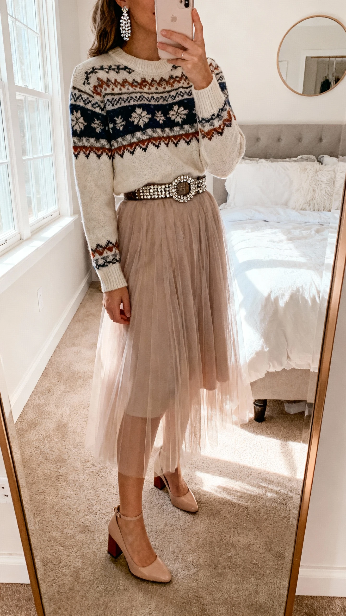 iPhone mirror selfie of a woman wearing a tulle skirt, Fair Isle sweater, embellished belt, sparkly earrings, and block-heel pumps, face not visible, bedroom mirror with soft morning window light, natural iPhone photo quality.