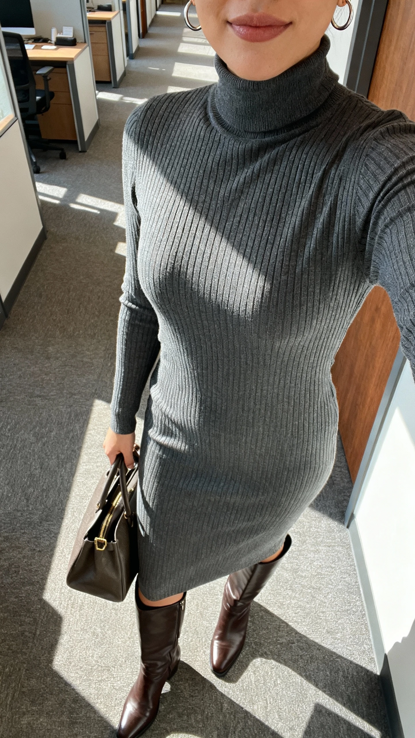iPhone selfie cropped at shoulders showing a woman in a sleek ribbed turtleneck midi dress with knee-high leather boots, minimal hoop earrings, structured tote, office hallway setting, face not visible, morning light, natural iPhone photo quality.