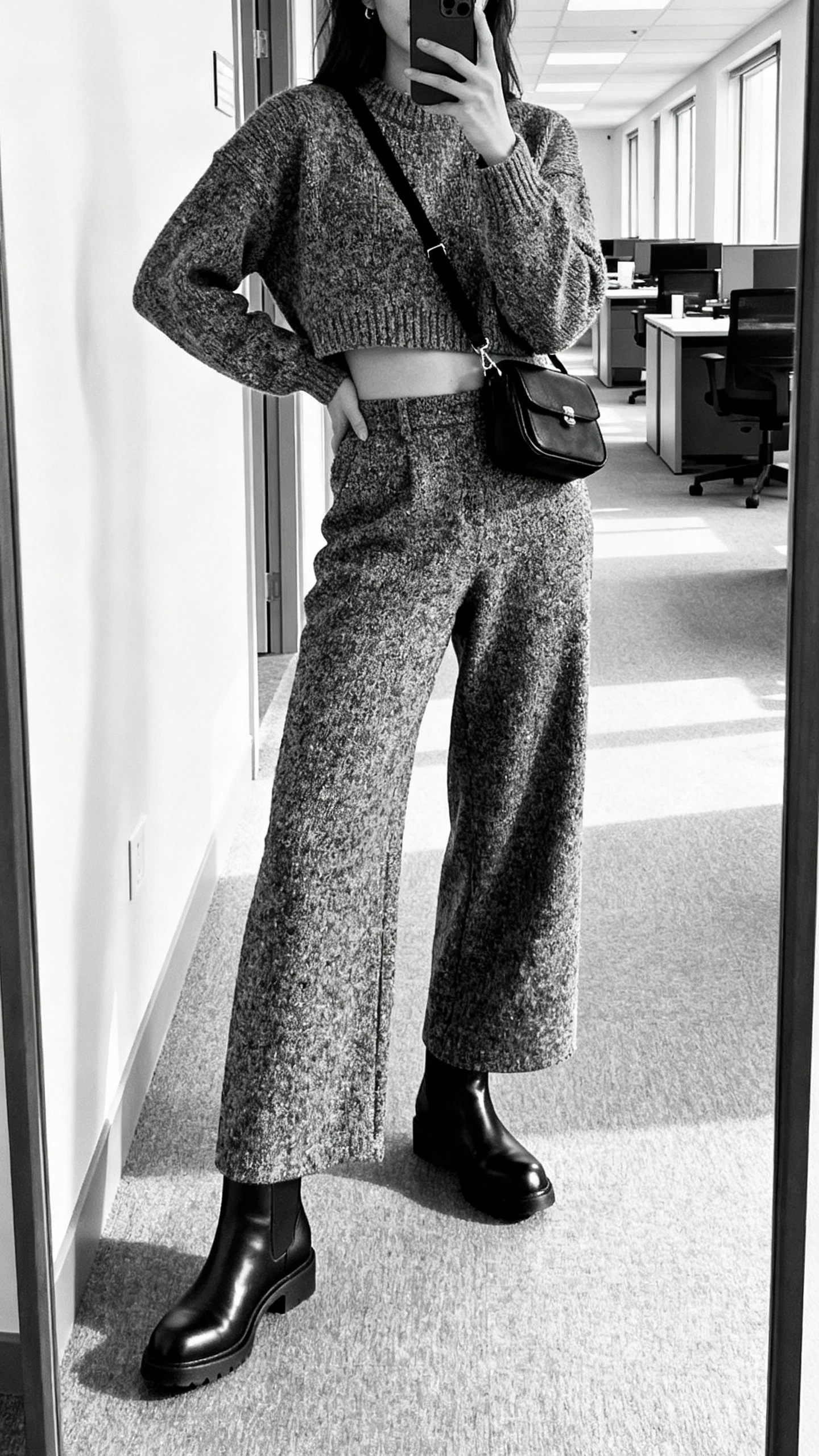 iPhone side-angle selfie of a woman in a textured monochrome look: cropped sweater, matching wide-leg trousers, sleek black Chelsea boots, small black crossbody, face not visible, office hallway mirror, bright indoor lighting, natural iPhone photo quality.