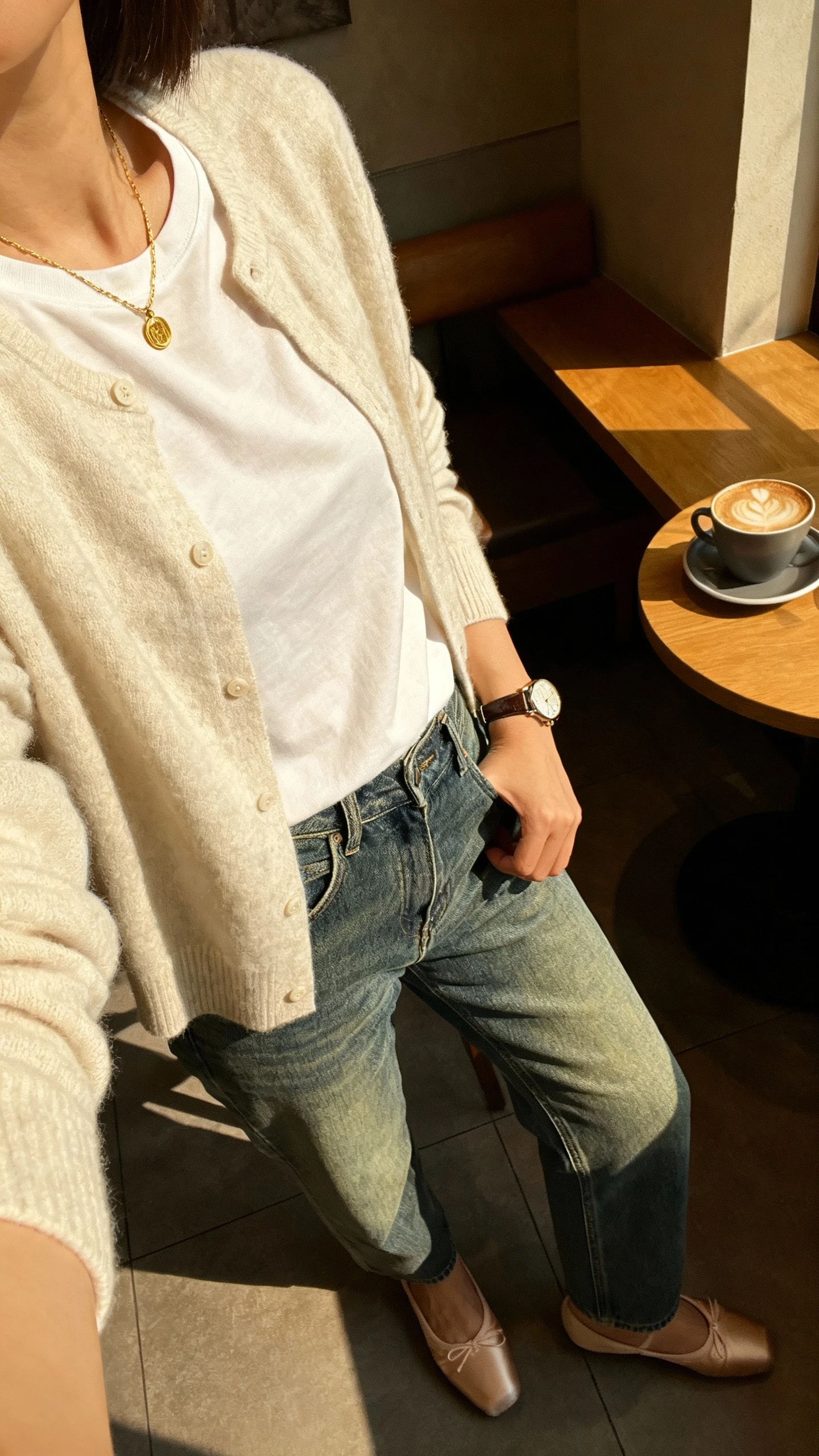 iPhone side-angle selfie of a woman wearing a soft cashmere cardigan layered over a simple tee, vintage straight denim, classic ballet flats, delicate gold necklace and watch, face not visible, taken in a sunlit coffee shop corner, natural iPhone photo quality.