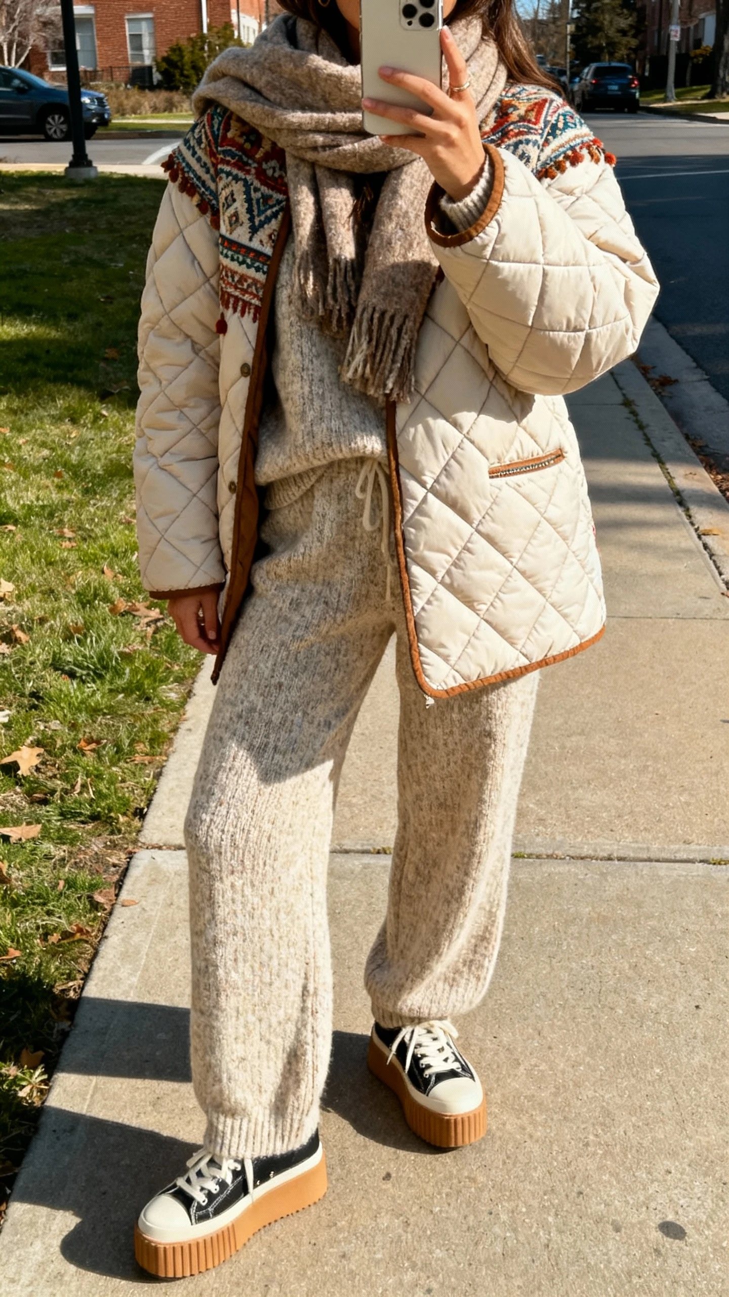 iPhone sidewalk selfie of a woman wearing a quilted boho puffer over a matching knit set (sweater and knit pants) with cozy scarf and platform sneakers, face not visible, natural daylight, casual iPhone aesthetic